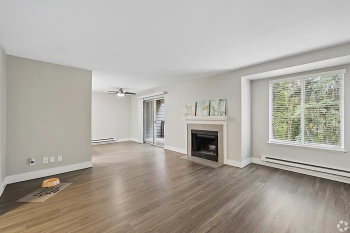 Bright and airy living room with elegant wood flooring, a stylish fireplace, large sunny window, and ceiling fan for comfort.