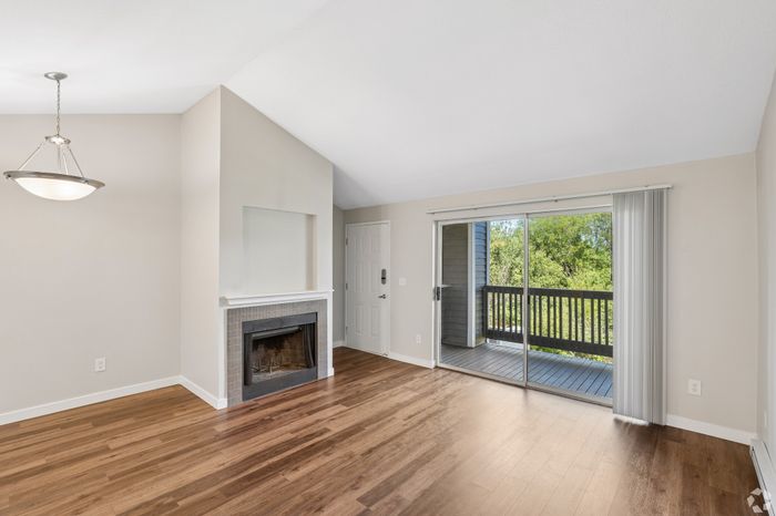 Bright and elegant living room with hardwood floors, featuring a cozy fireplace and a sliding glass door leading to a serene balcony view.