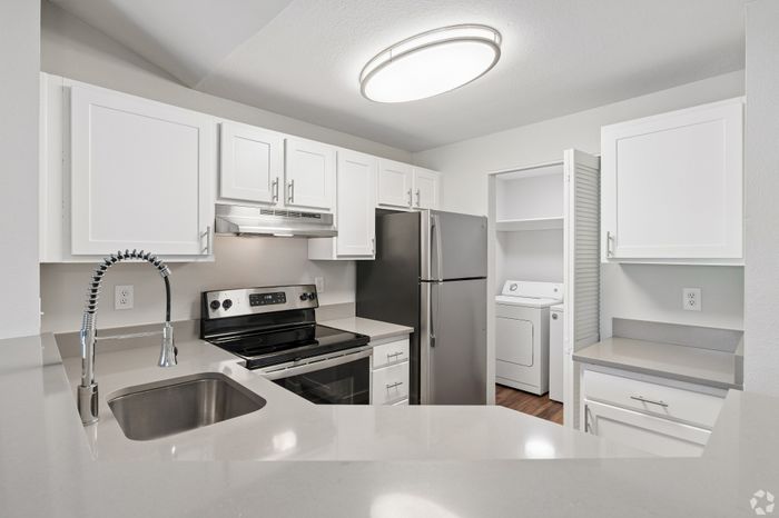 Modern kitchen with sleek stainless steel appliances and stylish white cabinetry, adjacent to a convenient laundry area.