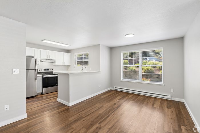 Modern bright open-concept kitchen and living area with sleek stainless steel appliances and large windows with garden views.