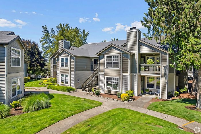 Charming apartment complex with stylish two-story buildings nestled in lush green landscaping, featuring spacious balconies and modern design.