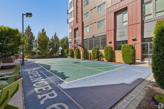 Modern apartment building with a well-maintained outdoor basketball court surrounded by lush greenery, perfect for recreational activities.