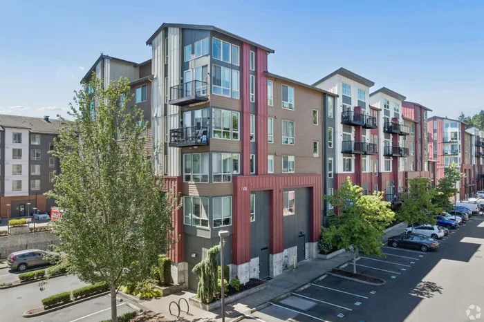 Modern apartment complex showcasing sleek architecture with large windows, private balconies, and vibrant exterior, surrounded by lush greenery and ample parking space.