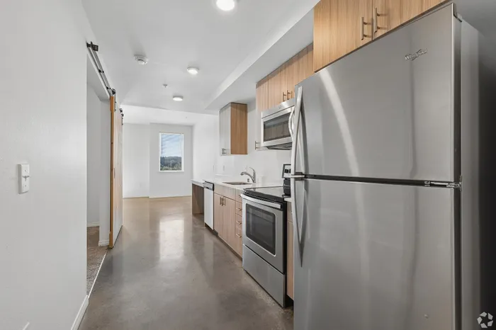 Modern kitchen with sleek stainless steel appliances, wooden cabinetry, and polished concrete floors basking in natural light from a large window.