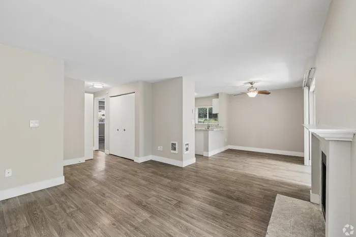 Inviting open-concept living space with modern wood flooring, a cozy fireplace, and ceiling fan for comfort.