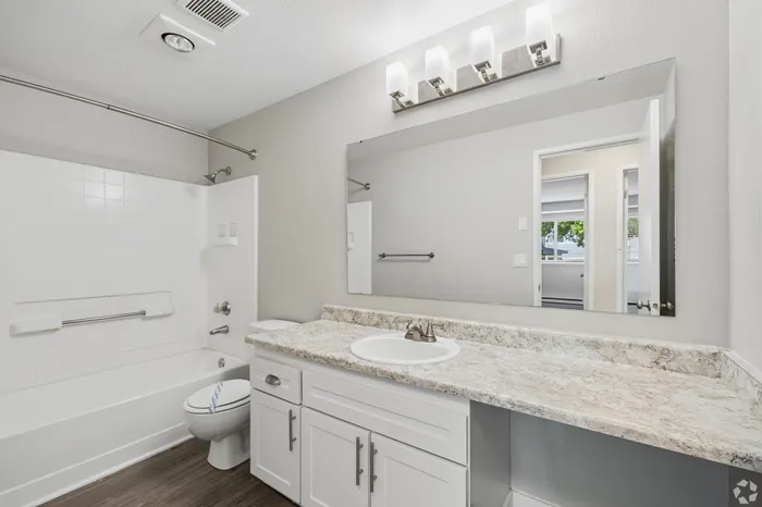 Modern bathroom featuring a sleek white countertop, large mirror, and bright vanity lights, offering a fresh and inviting atmosphere.