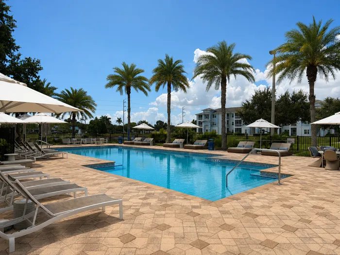 Luxurious outdoor pool area with sun loungers, palm trees, and a stunning backdrop of modern apartments.