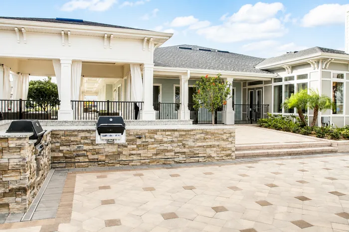 Luxurious outdoor area featuring elegant stone barbecue station, spacious tiled patio, and charming architectural details under a clear sky.