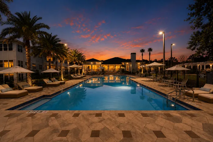 Luxurious resort-style pool area at sunset, featuring palm trees, comfortable sun loungers, and elegant lighting creating a serene atmosphere.