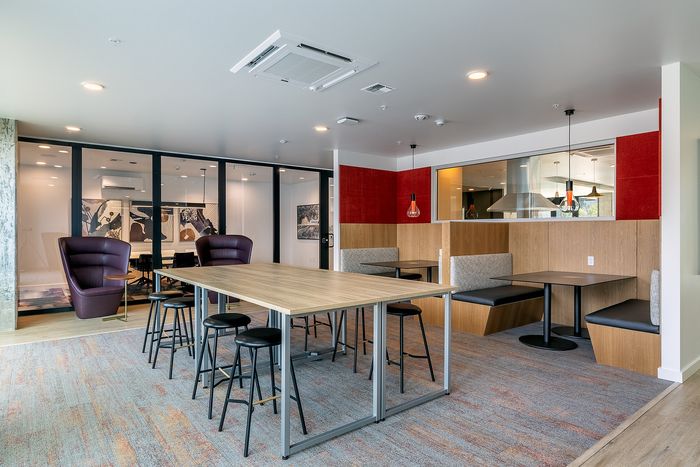 Modern co-working space featuring chic seating, vibrant red accents, and a spacious shared table ideal for collaboration.