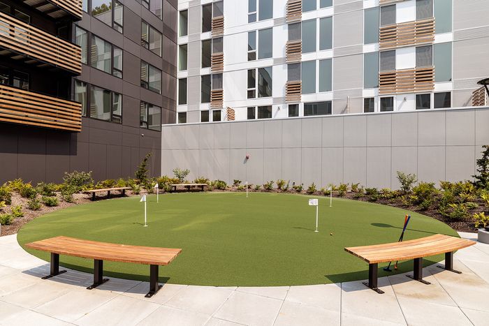 Modern urban apartment courtyard featuring a stylish putting green and sleek wooden benches, perfect for relaxation and leisure.