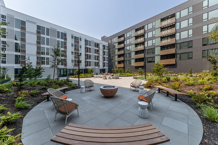 Modern apartment complex with elegant outdoor seating area, lush landscaping, and stylish facade.