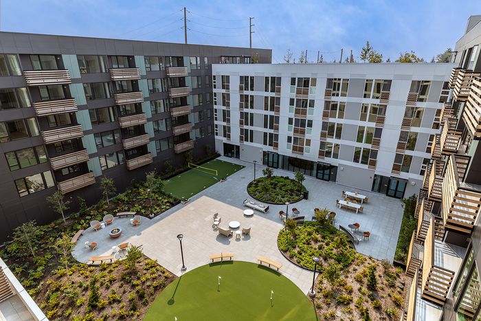 Modern apartment courtyard featuring a lush garden with seating areas, a mini golf course, and outdoor dining facilities, surrounded by contemporary multi-story buildings.