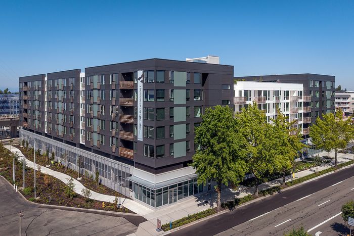 Modern urban apartment complex with sleek architecture, large windows, and lush greenery, offering convenient city living.