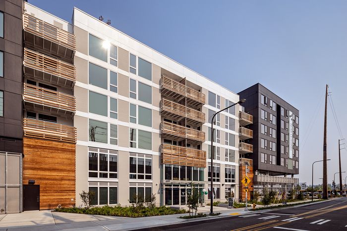 Contemporary apartment building with sleek design, featuring balconies and large windows, set in a vibrant urban area.