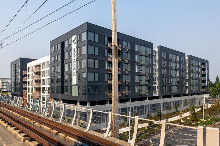 Modern urban apartment building with sleek architecture, large windows, and convenient rail access, now leasing.