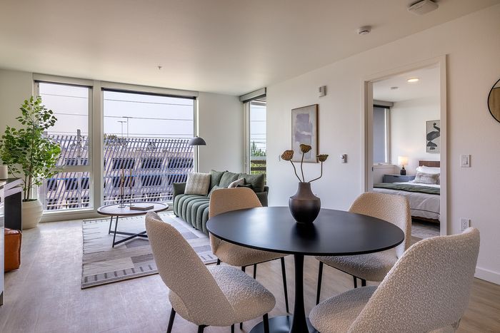 Modern living area with large windows, a chic green sofa, and stylish dining space adjacent to a cozy bedroom.