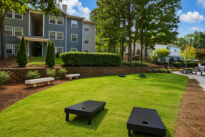 Charming apartment building with well-manicured lawn, cornhole boards, and inviting outdoor seating, surrounded by lush greenery.