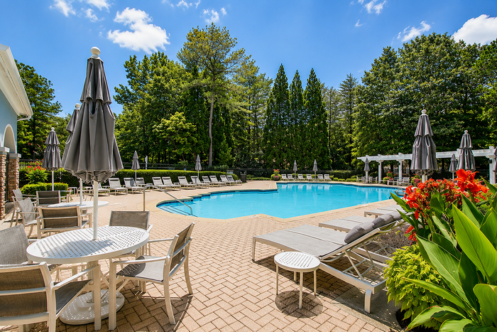 Inviting outdoor pool area with sun loungers, umbrellas, and lush greenery, ideal for relaxation and leisure on a sunny day.