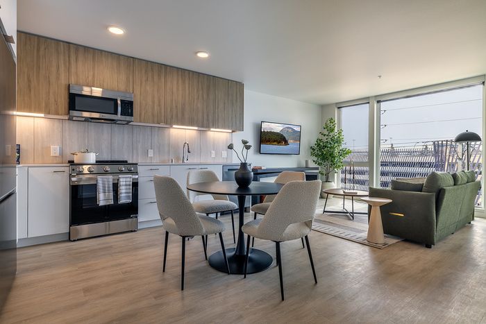 Modern open-plan living area with sleek kitchen, stylish dining set, and cozy lounge, featuring large windows with city views.