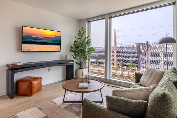 Modern living room with large windows offering a vibrant city view, cozy green sofa, and stylish decor.