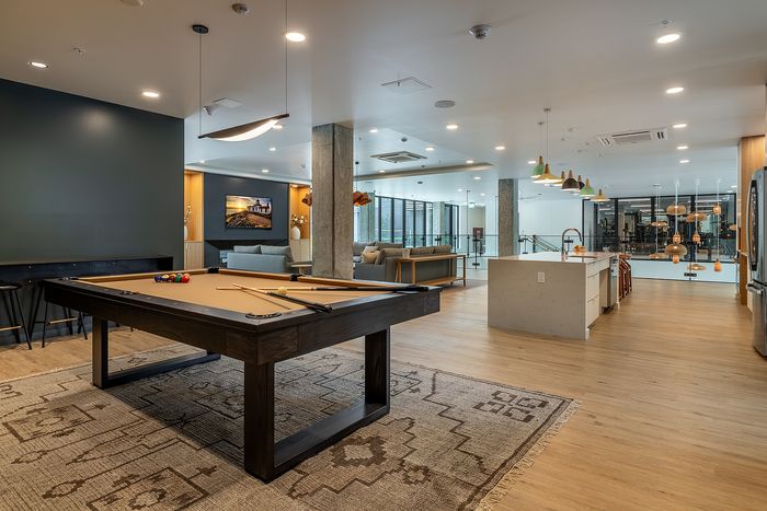 Modern living space featuring a stylish pool table, open-concept layout with a sleek kitchen island, comfortable seating area, and elegant lighting.