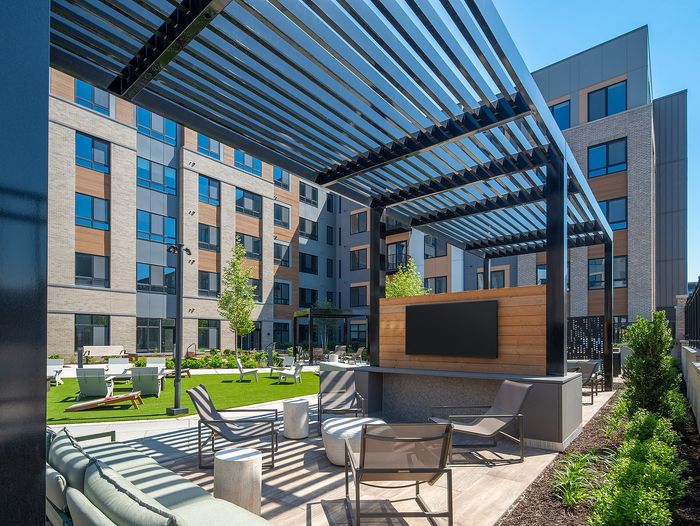 Modern apartment complex patio with stylish pergola, comfortable seating, and vibrant green lawn, perfect for relaxation and social gatherings.