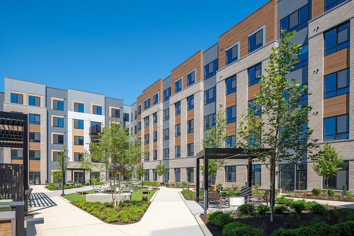 Modern apartment building with stylish facade and lush landscaped courtyard, featuring outdoor seating and vibrant greenery.