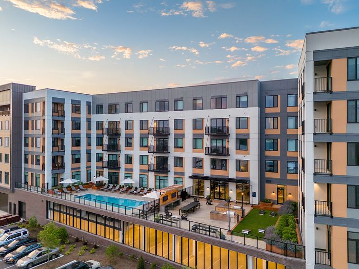 Modern apartment complex with a sleek design, featuring a rooftop pool and outdoor lounge area at sunset.