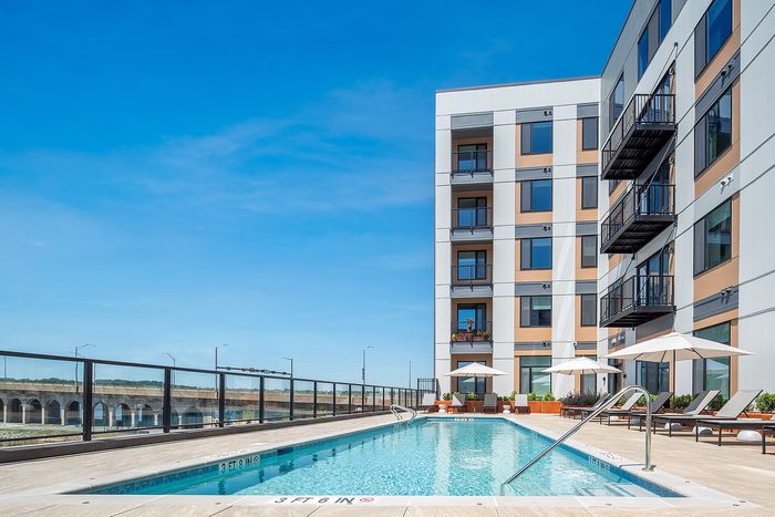 Modern apartment building with a luxurious rooftop pool, stylish lounge chairs, and umbrellas under a clear blue sky.