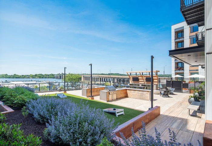 Luxurious rooftop patio with a scenic river view, featuring modern grills, lush landscaping, and stylish seating areas.