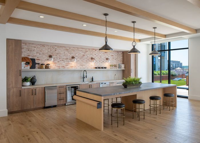 Modern kitchen with sleek wooden cabinetry, stylish pendant lighting, and a spacious island, overlooking a vibrant outdoor space through large glass doors.