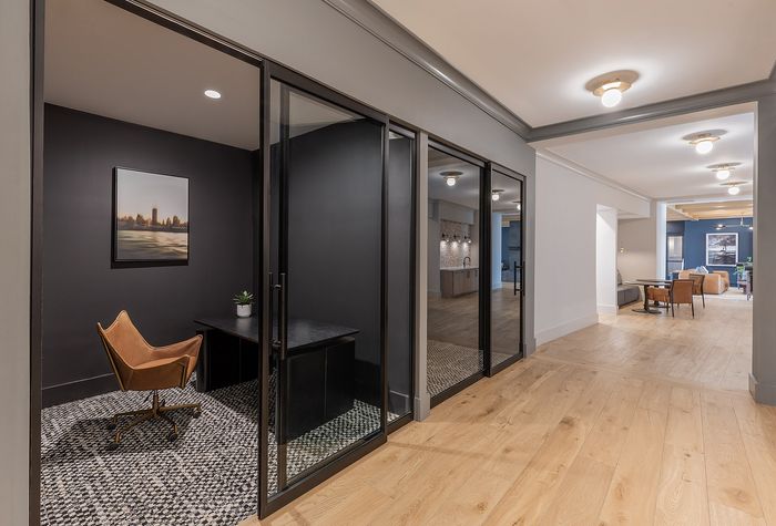 Sleek and modern office space with glass partitions, opening into a spacious and inviting living area featuring contemporary decor and warm wood flooring.