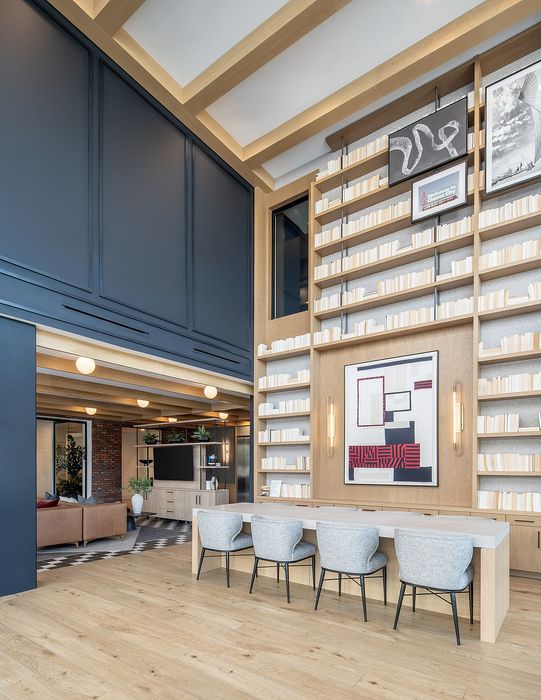 Chic open-plan interior highlighting a modern library with sleek shelving, elegant artwork, and a cozy seating area. Inviting living space with contemporary furnishings and natural lighting.