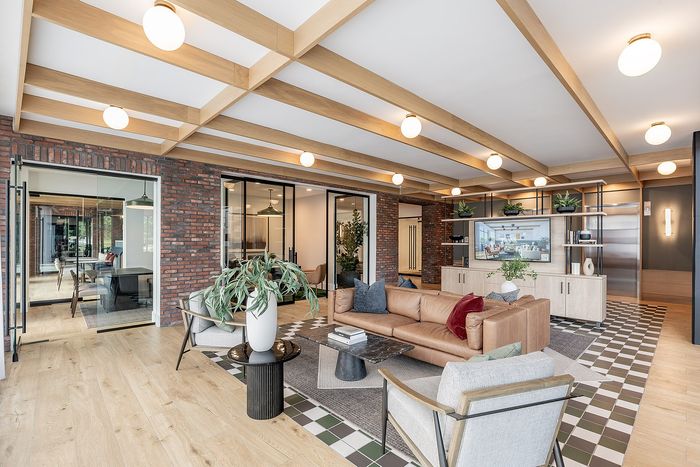 Modern living room featuring a leather sofa, elegant armchairs, and stylish wooden beams, complemented by brick accent walls and contemporary decor.