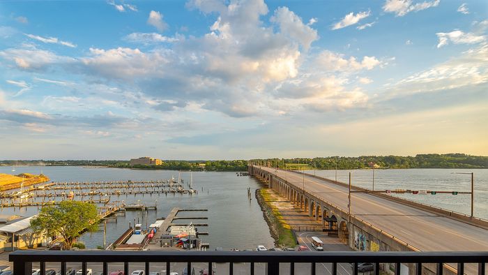 Breathtaking waterfront view from apartment balcony overlooking a serene river, elegant bridge, and picturesque marina at sunset.
