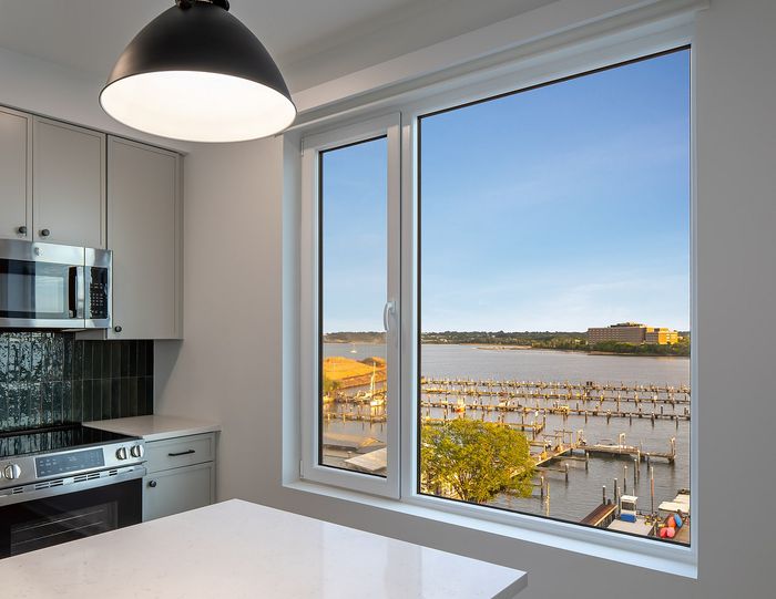 Chic kitchen with modern appliances and stunning waterfront view from large window, perfect for enjoying serene sunlit moments.