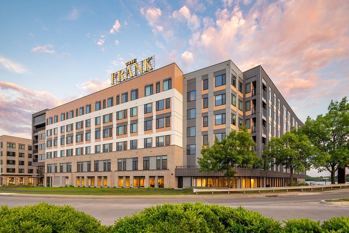 Modern apartment complex with vibrant exterior design, surrounded by lush greenery and highlighted by a beautiful sunset sky.