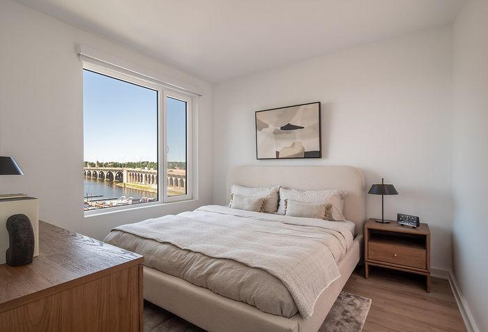 Bright, modern bedroom with a cozy bed, elegant decor, and a stunning river view through a large window.