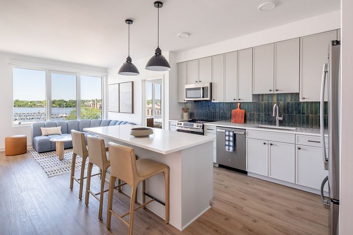 Modern open-plan kitchen and living area with sleek design, featuring a cozy seating area, large windows with a waterfront view, and stylish pendant lighting.