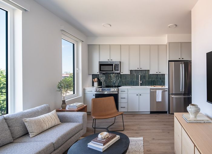 Contemporary apartment interior with a stylish open-plan kitchen and living area, featuring large windows and sleek cabinetry.
