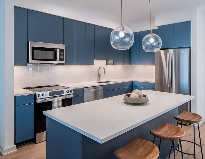 Modern kitchen with sleek blue cabinetry, stainless steel appliances, and elegant pendant lighting over a spacious island.