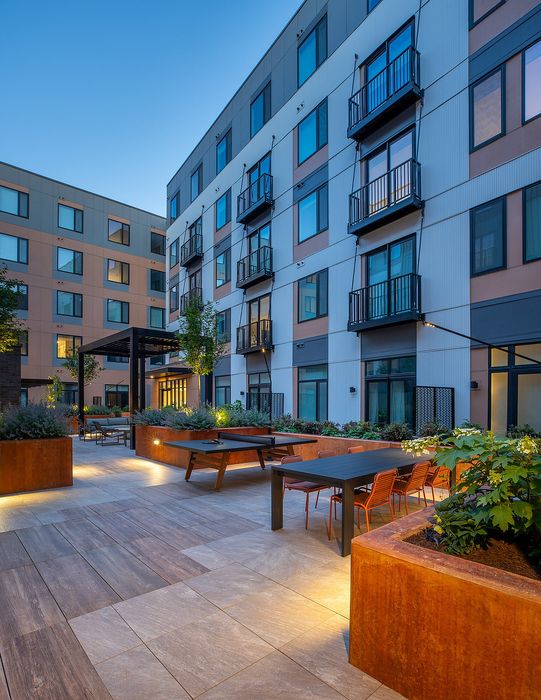 Chic apartment complex featuring a beautifully landscaped outdoor terrace with modern seating and ambient lighting at dusk.