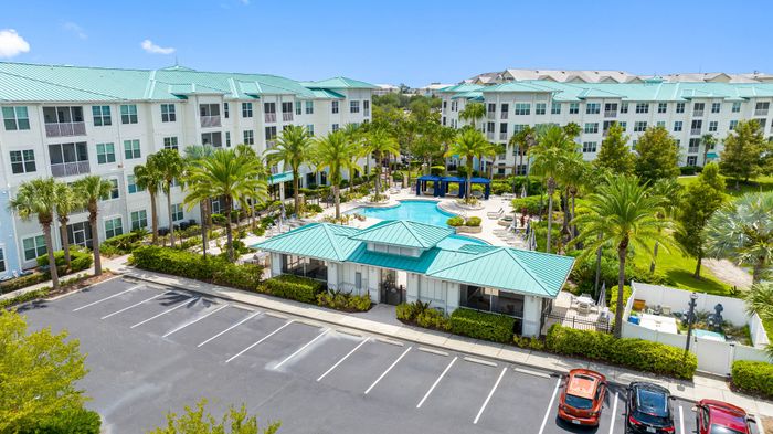 Luxurious apartment complex with lush landscaping, sparkling pool area, and modern architecture featuring teal rooftops and inviting outdoor spaces.