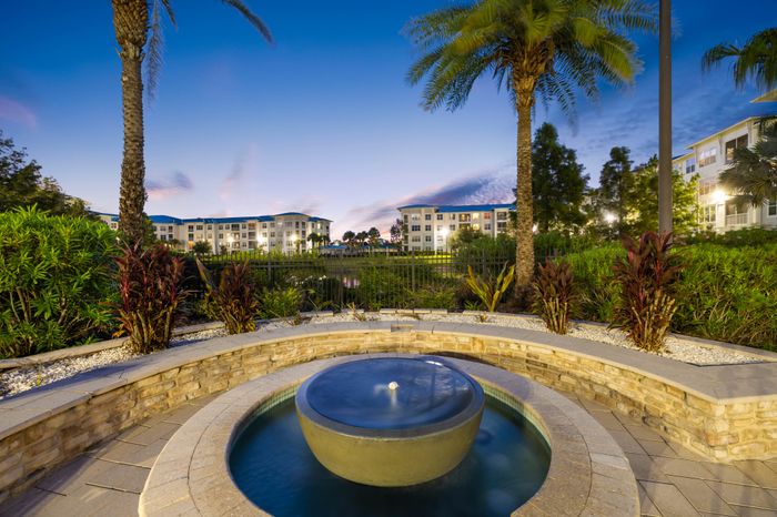 Gorgeous sunset view from a luxury apartment complex, featuring a tranquil circular fountain, lush landscaping, and elegant architecture.