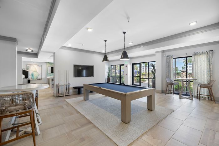 Chic modern recreation room with a pool table, stylish seating, and large windows offering lush garden views.