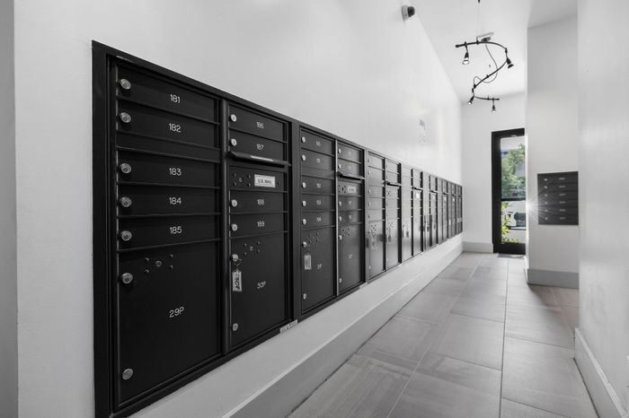 Chic apartment mailroom featuring sleek black mailboxes with modern lighting and a bright entryway.