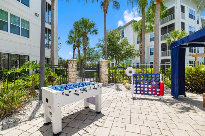 Inviting outdoor recreation area featuring a foosball table and giant Connect Four game surrounded by lush landscaping and modern apartment buildings.
