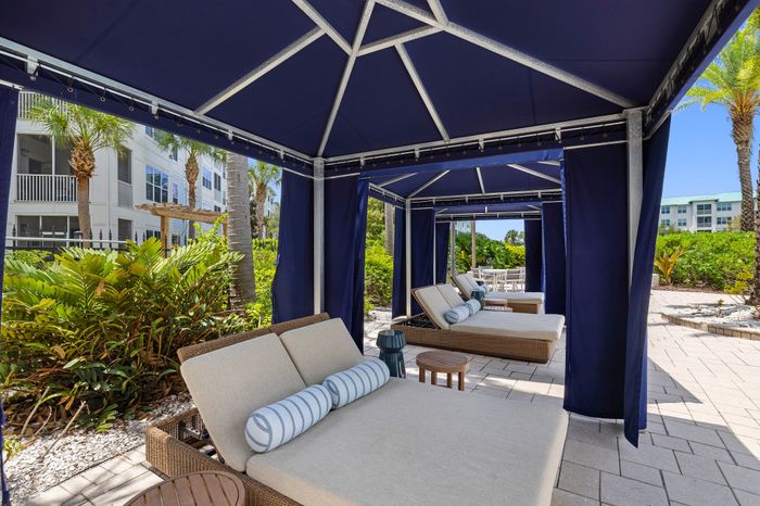 Luxurious outdoor cabanas with plush loungers and elegant blue canopies, offering a relaxing retreat amidst lush greenery and sunny views.