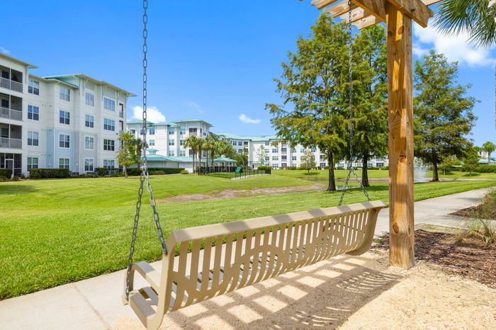 Inviting garden view from a charming apartment courtyard featuring a cozy swing, lush green lawns, and elegant multi-story buildings under a bright blue sky.